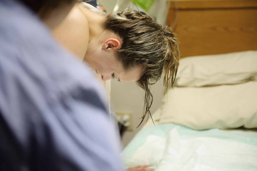 Mother in Labor Kvinde med vådt hår under fødsel, bøjet over seng, i fødselsposition.