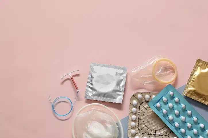 Forskellige præventionsmidler som spiral, p-piller og kondomer på pink baggrund.